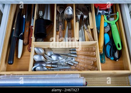 Wooden cutlery tray is divided into compartments and placed in drawer of kitchen table. Stock Photo