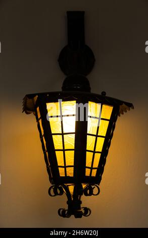 Wall lamp with classic design, lantern look. The lantern-like lamp hangs on the wall and the light is on. Stock Photo