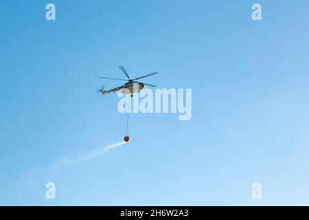 Wildfire helicopter going to fire area to extinguish forest fire.  Wildfire helicopter with a water bucket on a blue sky. Stock Photo