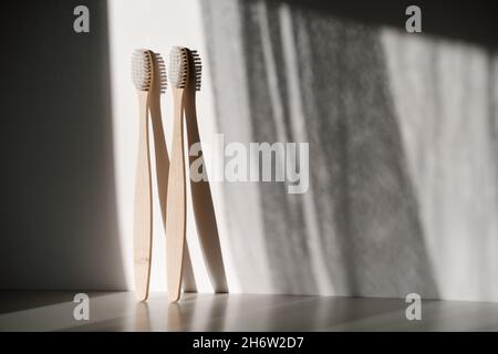 two light wood bamboo eco recyclable toothbrushes standing vertical with white bristles on white background and morning shadows Stock Photo