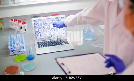 close-up of a computer screen with molecules on a laboratory bench next to vials, test tubes and blood samples. And two researchers pointing and analy Stock Photo