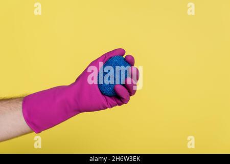 partial view of man in rubber glove holding blue dish scrubber isolated on yellow Stock Photo