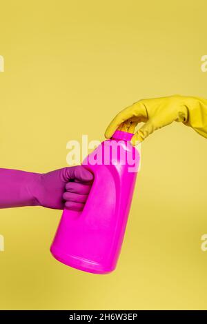 cropped view of people in rubber gloves holding pink bottle with detergent isolated on yellow Stock Photo