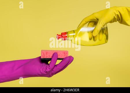 cropped view of people in rubber gloves holding bottle with detergent and sponge isolated on yellow Stock Photo