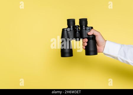 cropped view of man holding black modern binoculars on yellow Stock Photo