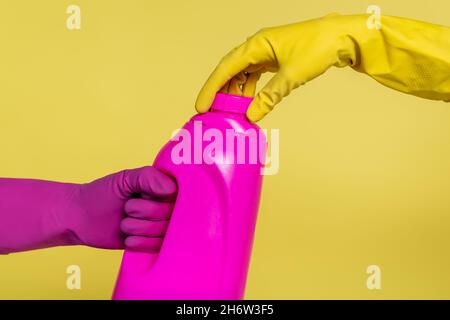 cropped view of people in rubber gloves holding bottle with detergent isolated on yellow Stock Photo