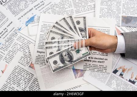 KYIV, UKRAINE - NOVEMBER 1, 2021: top view of man holding dollar banknotes above printed newspapers Stock Photo