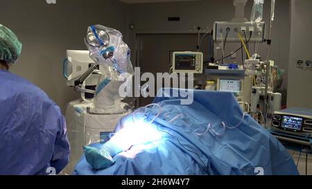 Close-up of a doctor in an operating room surrounded by machines or robots, and with a patient on the operating table waiting for surgery Stock Photo