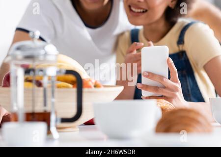 cropped view of happy interracial couple using smartphone during breakfast Stock Photo