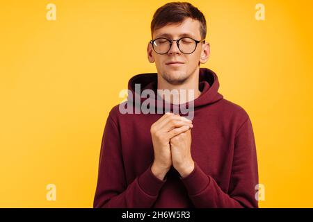 person praying hopes for the best, with hands in prayer position. Asking God for good luck, success, forgiveness on an isolated yellow background. The Stock Photo