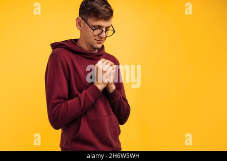 person praying hopes for the best, with hands in prayer position. Asking God for good luck, success, forgiveness on an isolated yellow background. The Stock Photo