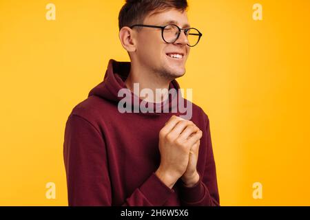 person praying hopes for the best, with hands in prayer position. Asking God for good luck, success, forgiveness on an isolated yellow background. The Stock Photo