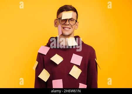 Young sad, tired, exhausted, frustrated, sleepy worker, Man in a hurry. this guy has stickers on his sweater and forehead. isolated on yellow backgrou Stock Photo