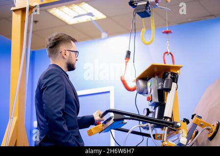 Worker engineer uses vacuum conveyor to move flat load in factory. Stock Photo