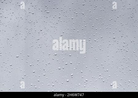 Rain drops on window glasses surface with gray sky background. Natural backdrop of raindrops. Abstract overlay for design. The concept of bad rainy we Stock Photo