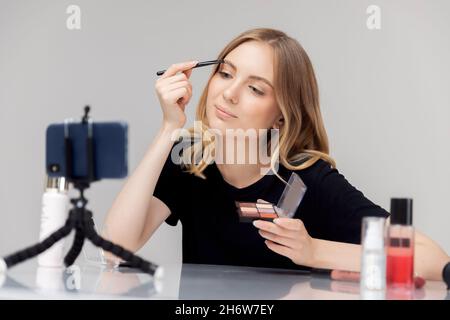 Influencer young woman beauty blogger records video tutorial of course on facial skin and eyebrow care on phone. Stock Photo