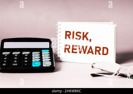 Text word risk and rewards on a notebook, next to a calculator and glasses on a light background. Concept of risk, analysis of reward in business Stock Photo