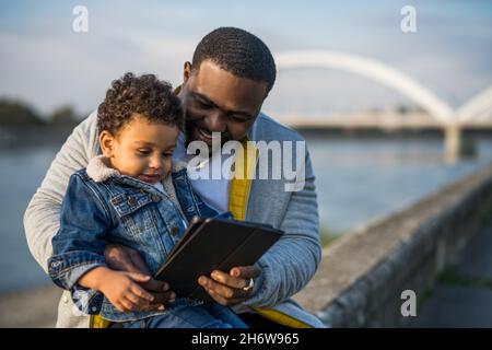 Father and his son using digital tablet while sitting together outdoor. Stock Photo