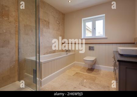 Newmarket, Suffolk, England - September 23 2019: New fitted bathroom in British family home with marble tiled walls and floors, bath tub, basin and wc Stock Photo