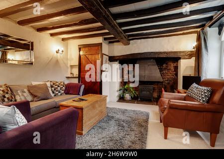 Kedington, Suffolk, November 19 2019: Furnished Traditional English cottage living room or lounge with exposed beams and fireplace with wood burner Stock Photo