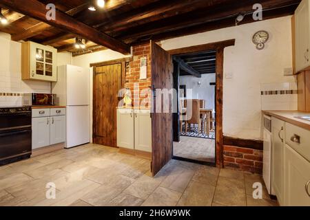 Kedington, Suffolk, November 19 2019: Sparsely furnished cottage kitchen with exposed ceiling beams and brick wall. Doorway open to Dining room. Stock Photo