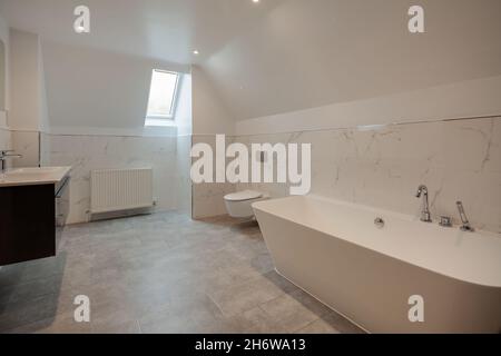 Clavering, England -  April 6 2020: Well lit bathroom within recently completed new home prior to sale with bath tub, wall mounted cupboard and basins Stock Photo