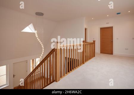 Clavering, England -  April 6 2020: New Home entrance and reception hall with wooden floor and carpeted oak staircase rising to first floor landing Stock Photo