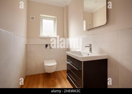 Clavering, England -  April 6 2020: New Home Cloakroom or washroom with wall hung wc toilet and sink with tiled walls and timber floor Stock Photo