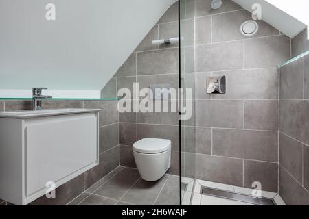 Cambridge, England - July 31 2019: Shower room with tiled floor and walls with sloping roof, toilet and wash handbasin Stock Photo