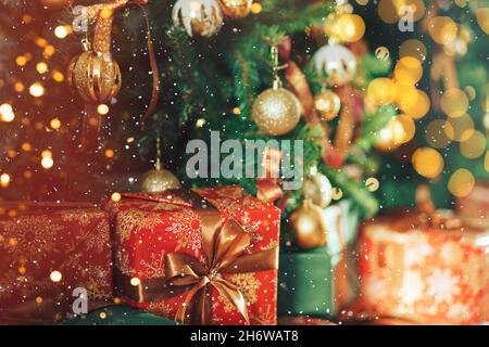 Many gift boxes standing under decorated Christmas tree with superimposed falling snow Stock Photo