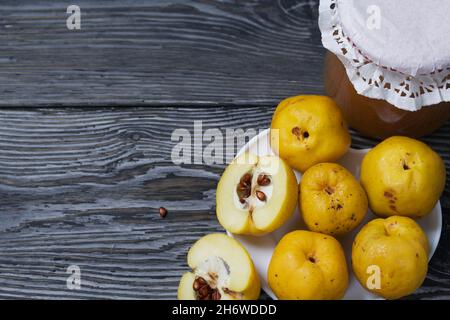 Quince fruits on a plate. Quince jam. The yellow fruit is cut, the seeds are visible. Plate on black pine boards. Close-up shot. Stock Photo