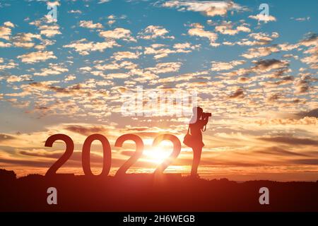Silhouette of photographer taking photos in 2022 years at sunrise or sunset background. Idea for happy new year 2022. Stock Photo