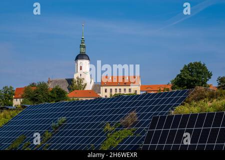 Photovoltaik solar panels arranged on the slope of a hill in front of the small medieval town. Stock Photo