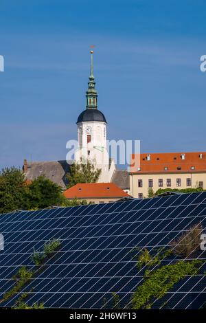 Photovoltaik solar panels arranged on the slope of a hill in front of the small medieval town. Stock Photo