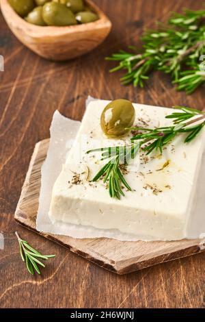 Cheese feta with rosemary, herbs, olives and olive oil on wooden cutting board on old wooden background. Traditional Greek homemade cheese. Selective Stock Photo