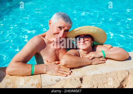 Senior retired family couple relaxing in resort swimming pool. Happy people enjoying summer vacation in tropical hotel. All inclusive. Stock Photo