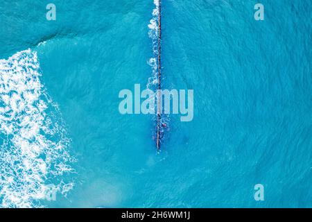 Aerial top view of breakwater with wave of sea, clean blue water around beach. Stock Photo