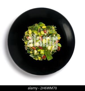 stir fried leeks with red chilies and onions, green vegetarian dish on a black plate, isolated on white background, taken from above Stock Photo