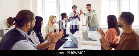 Happy young man gives high five to colleague while diverse business team is applauding Stock Photo