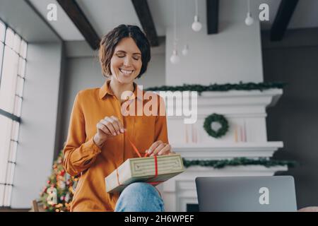 Happy young Spanish woman engaged in packing Xmas gifts at home during Christmas holidays Stock Photo