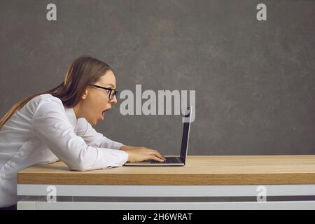 Profile view of a shocked young woman looking at the screen of her laptop computer Stock Photo