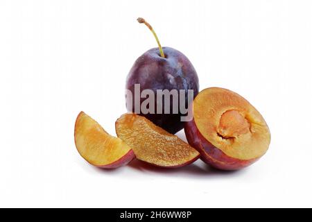 purple plum with plum slices lying next to it, isolated on a white background Stock Photo
