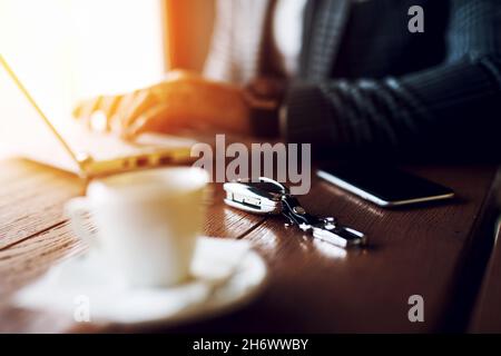Closeup of car keys, smartphone and white coffee cup lying on wooden table in cafe Stock Photo