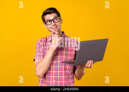 Photo of cheerful young happy man look empty space think hold laptop freelancer isolated on yellow color background Stock Photo