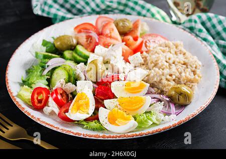 Breakfast oatmeal porridge with greek salad of tomatoes, cucumbers, olives, feta cheese and eggs. Healthy balanced food. Stock Photo