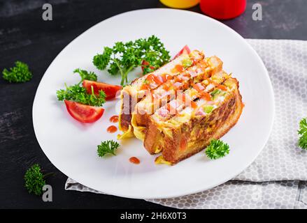 Roasted sandwich cheese,hm, peppers and scrambled eggs on white plate. Dark background. Stock Photo
