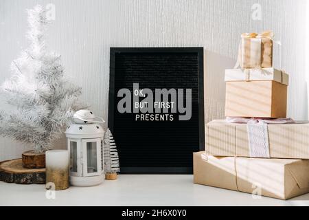 Many craft Christmas gift boxes and black letter board with quote Ok but first presents. Festive Christmas letter board ideas and quotes. Blackboard Stock Photo