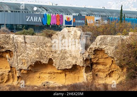 View of the Kings Avenue Mall shopping centre facade and advertising signage rising above the Neo Pafos archaeological site, Paphos, Cyprus Stock Photo