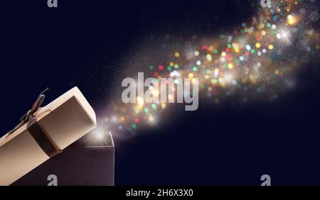Golden open gift box with magic lights on deep dark blue background. Holiday's spirit concept. Stock Photo