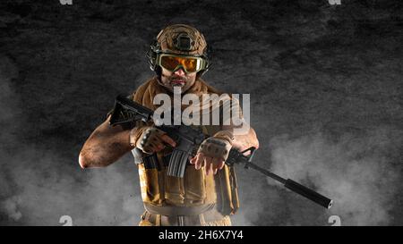 An armed mercenary soldier, shrouded in smoke, stands against the background of a dark concrete wall. Modern warfire concept. Stock Photo